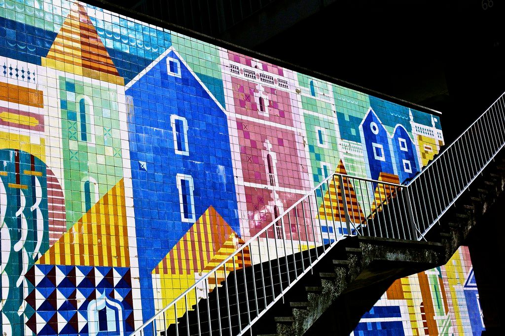 A picture of the side of a building covered in brightly colored tiles depicting a neighborhood.